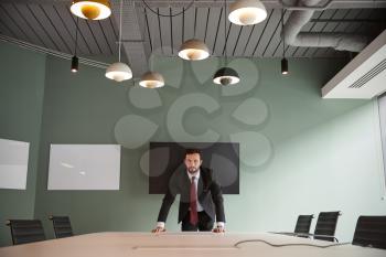 Portrait Of Young Businessman Leaning On Boardroom Table At Graduate Recruitment Assessment Day In Office