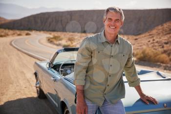 Senior white man leaning on open top car at desert roadside