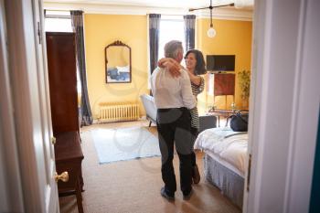 Mature couple embrace, looking at each other, in hotel room
