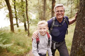 Grandfather and grandson taking a break while hiking together in a forest, close up, smiling to camera