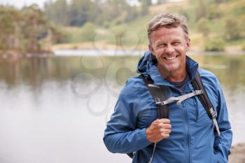Adult man on a camping holiday standing by a lake smiling to camera, close up, Lake District, UK