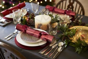Close up of Christmas table setting with Christmas crackers arranged on plates and red and green table decorations, elevated view