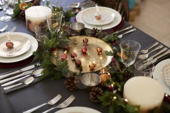 Christmas table setting with bauble name card holders arranged on plates, golden plate centrepiece with baubles, and green and red table decorations, elevated view