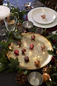 Christmas table setting with baubles on golden plate, bauble name card holder arranged on plate and green and red decorations, close up