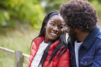 Happy black couple leaning on a fence in the countryside looking into each others eyes, close up