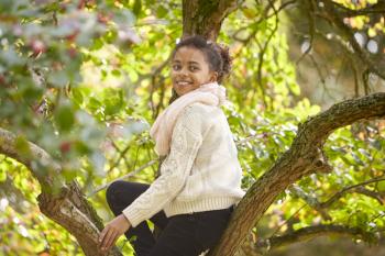 Young girl sitting in an Autumn tree, turning and smiling to camera, side view