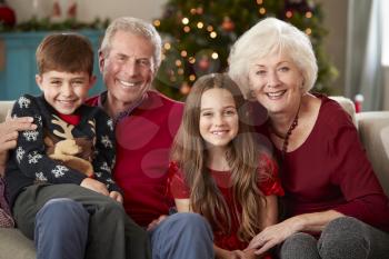 Portrait Of Grandparents With Grandchildren Sitting On Sofa In Lounge At Home On Christmas Day