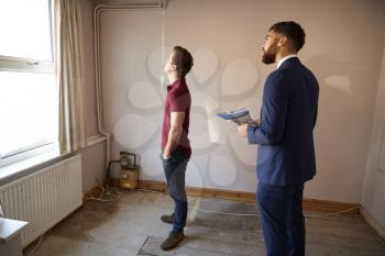 Male First Time Buyer Looking Around House For Renovation With Realtor