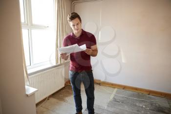 Male First Time Buyer Looking At House Survey In Room To Be Renovated