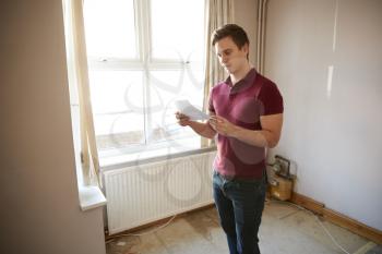 Male First Time Buyer Looking At House Survey In Room To Be Renovated