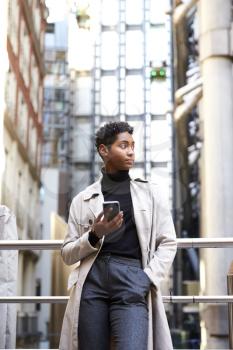 Fashionable young black woman leaning on handrail in the city area holding smartphone, low angle, close up, vertical
