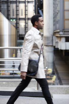 Side view of a young black businessman walking in a street in the city, London UK, motion blur