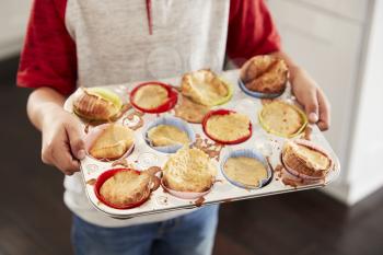 Boy holding baking tray, presenting the cakes he has baked to camera, mid section, close up