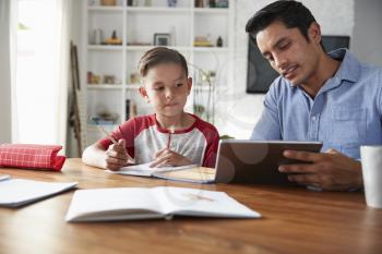 Hispanic pre-teen boy sitting at table working with his home school tutor, using tablet computer