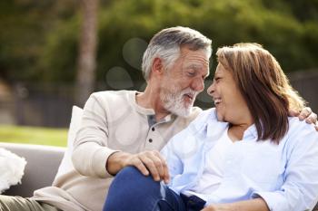 Senior couple sitting on a seat in the garden, heads turned smiling to each other