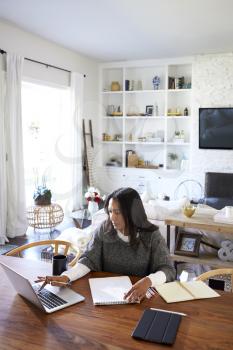 Elevated view of middle aged mixed race woman sitting at the table in her dining room using a laptop computer, vertical