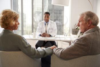 Senior Couple Having Consultation With Male Doctor In Hospital Office