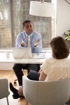 Male Financial Advisor In Modern Office Sitting At Desk Meeting Female Client