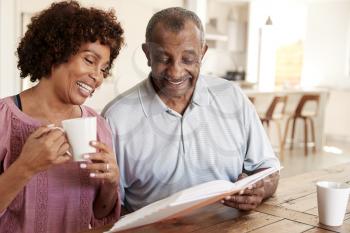 Middle aged black woman and her dad looking through photo album together at home, close up