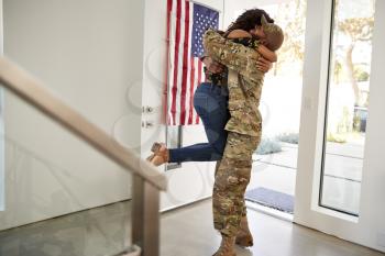 Returning millennial black soldier lifting his wife off her feet in their home, side view