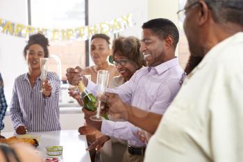 Middle aged black man opening champagne to celebrate with his three generation family, close up