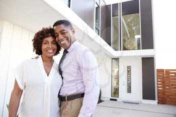 Middle aged black couple stand outside admiring their modern home, back view