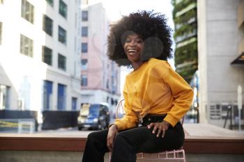 Young black woman with afro hair sitting on a chair in the street laughing to camera