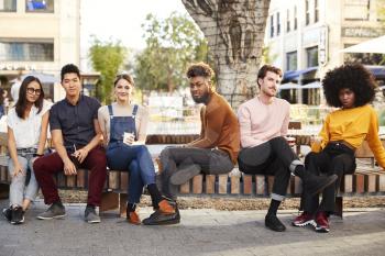 Six millennial hipster friends in the city relaxing by a fountain with drinks, smiling to camera