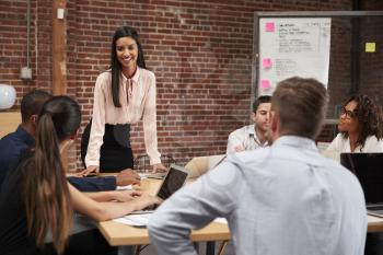 Young Businesswoman Standing And Leading Office Meeting Around Table