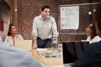 Mature Businessman Standing And Leading Office Meeting Around Table