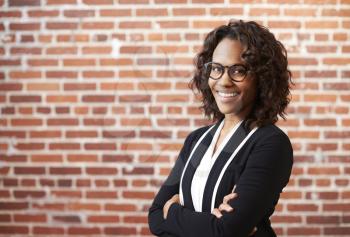 Portrait Of Smiling Businesswoman Wearing Glasses Standing Against Brick Wall In Modern Office