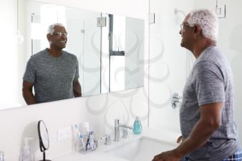 Smiling Senior Man Looking At Reflection In Bathroom Mirror Wearing Pajamas