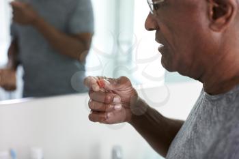 Close Up Of Senior Man In Bathroom Mirror Wearing Pajamas Taking Vitamin Supplement Tablet