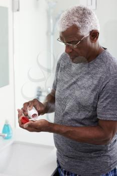Senior Man In Bathroom Mirror Wearing Pajamas Taking Vitamin Supplement Tablet