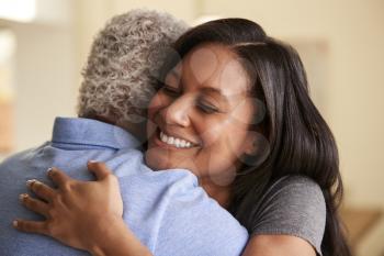 Over The Shoulder View Of Senior Father Being Hugged By Adult Daughter At Home