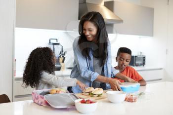 Children In Kitchen At Home Helping Mother To Make Healthy Packed Lunch