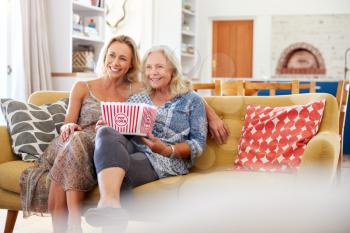 Mother With Adult Daughter Eating Popcorn Watching Movie On Sofa At Home Together