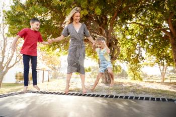 Mother Playing With Children On Outdoor Trampoline In Garden