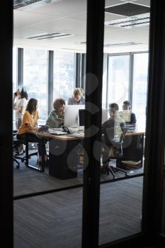 Creative business team working in a casual office, seen from doorway through glass wall, vertical