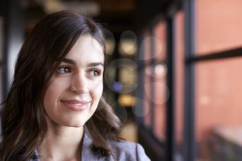 Millennial white businesswoman looking out of the window in an office, head and shoulders