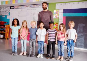 Portrait Of Elementary School Pupils Standing In Classroom With Male Teacher
