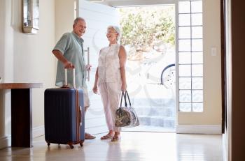 Senior Couple Standing By Front Door With Suitcase About To Leave For Vacation