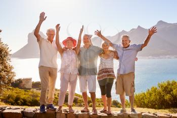 Portrait Of Senior Friends Visiting Tourist Landmark On Group Vacation With Arms Raised