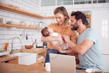 Busy Family In Kitchen At Breakfast With Mother Caring For Baby Son