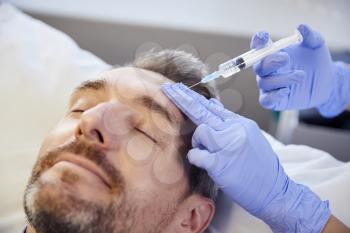 Female Beautician Giving Mature Male Patient Botox Injection In Forehead