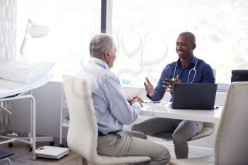 Senior Male Patient In Consultation With Doctor Sitting At Desk In Office
