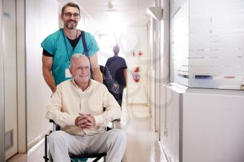 Male Orderly Pushing Senior Male Patient Being Discharged From Hospital In Wheelchair