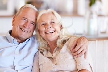 Happy senior white couple sitting at home embracing and smiling to camera, front view, close up