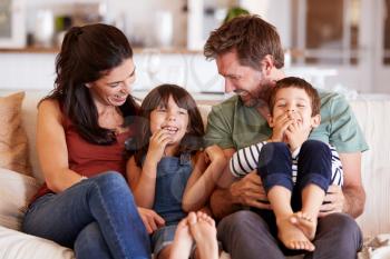 Mid adult white couple and their two young children sitting on a sofa at home smiling at each other