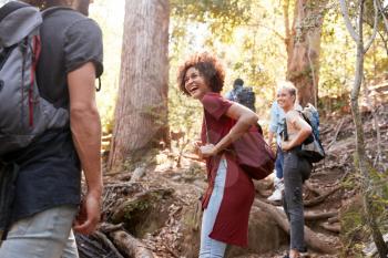 Millennials hiking up a forest trail turning around to look back at friends, three quarter length